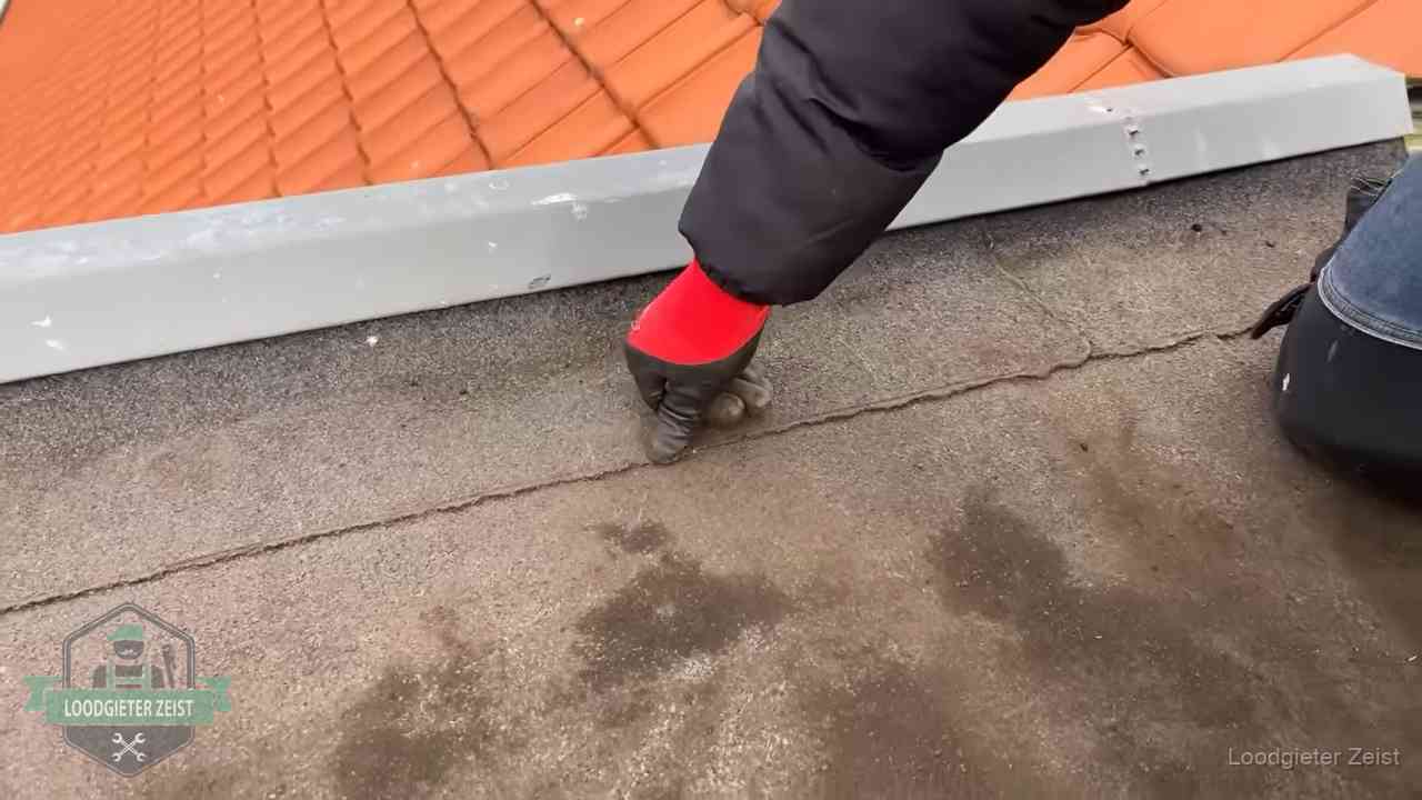 Vakman wijst een naad met vochtplekken aan op een bitumen plat dak in Zeist