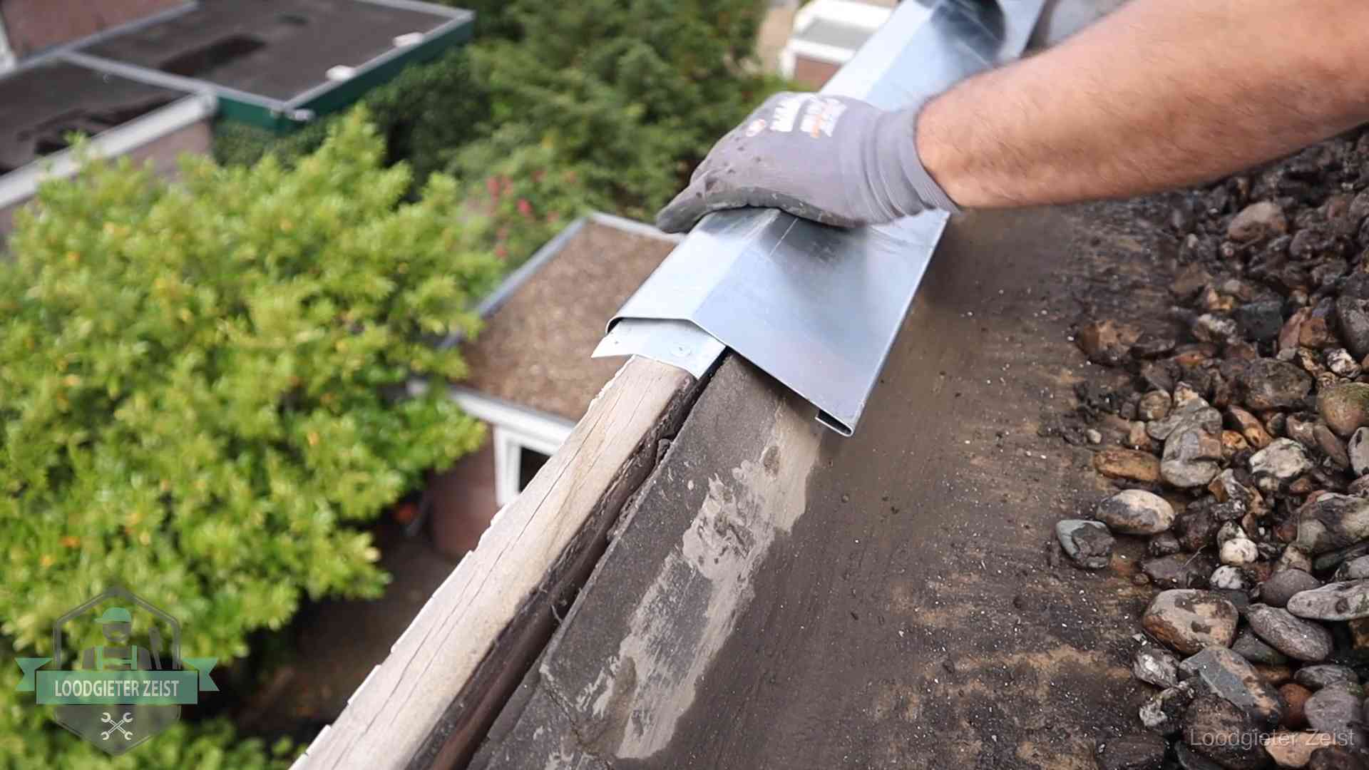 Dakdekker plaatst een zinken deklijst op een dakrand met uitzicht over een woonwijk in Zeist