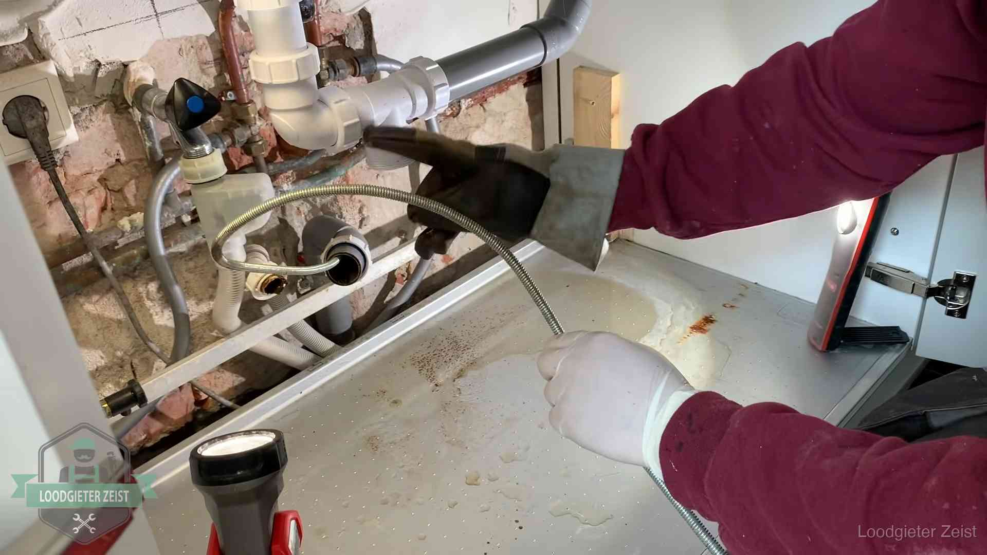 Ontstoppingsveer gaat in een geopende sifonaansluiting onder het aanrecht in Zeist